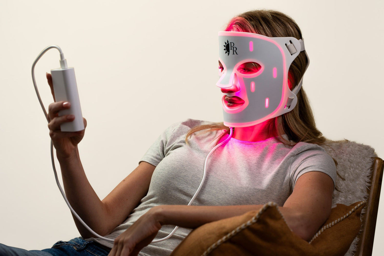 Person wearing a LED face and neck mask with visible branding, holding a power source.